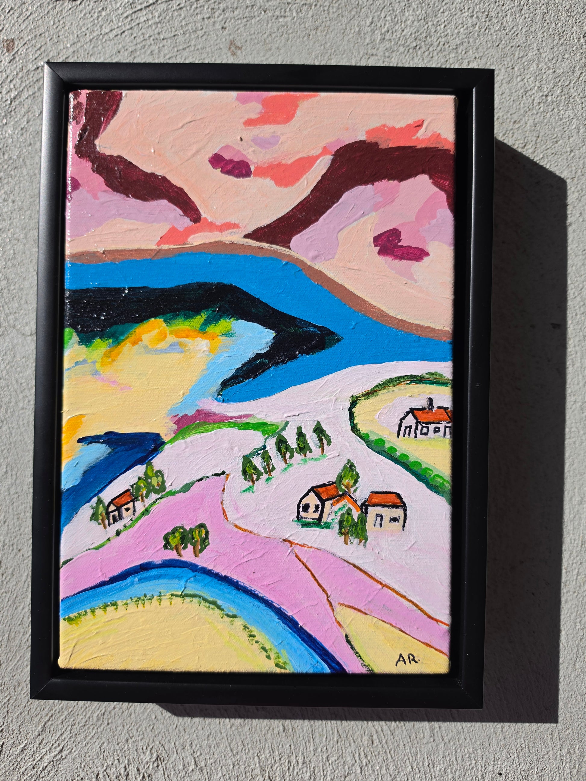 Colourful framed abstract landscape painting with houses, rolling hills and a winding blue river by Alpana Rai